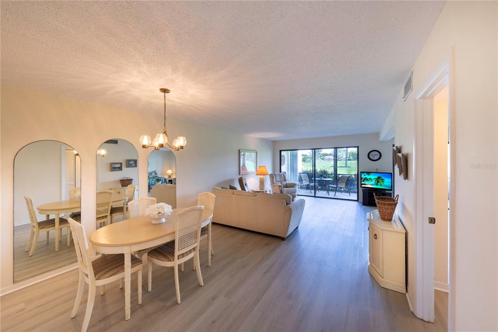 A dining area and living room with light wood-look flooring and a sliding glass door — 696 BIRD BAY DRIVE W UNIT 138, VENICE, FL