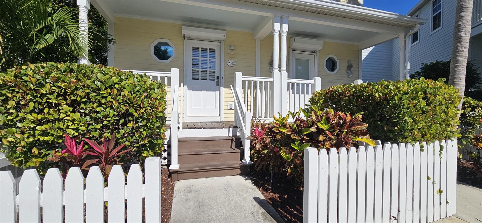 A yellow house with a white picket fence, front porch, and stairs leading to the entrance — 2002 Marina Villa Drive, FL 33050, FL