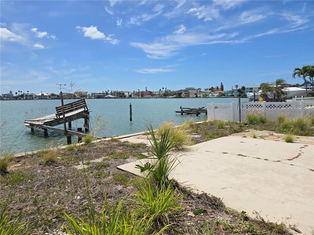 A waterfront view of a dilapidated wooden dock and a concrete patio under a blue sky — 249 144TH AVENUE, MADEIRA BEACH, FL