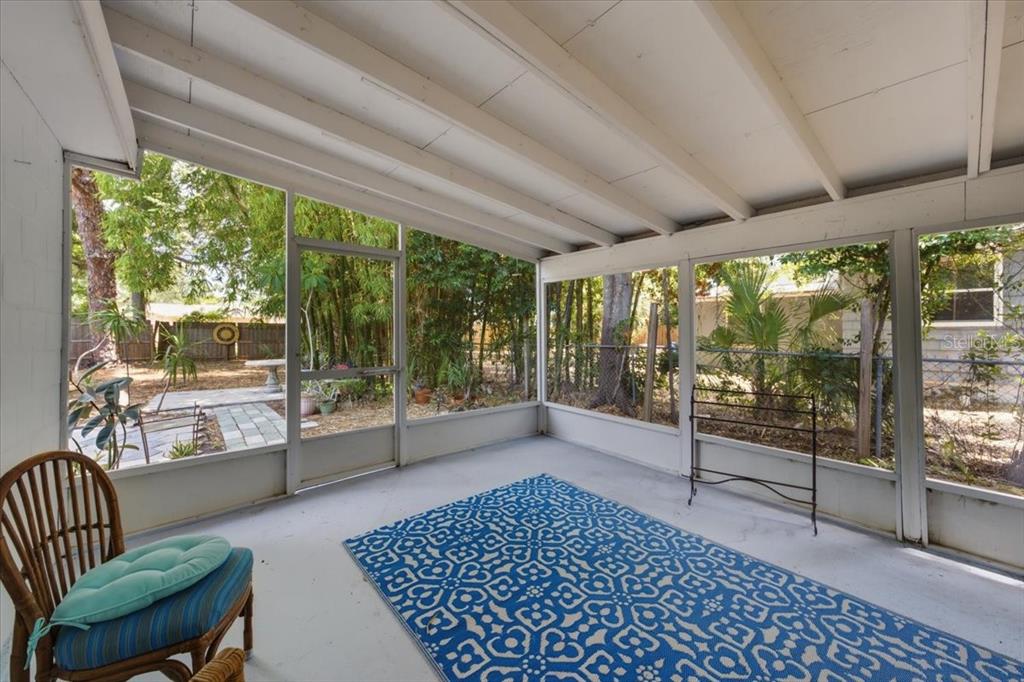 A screened-in porch with a blue patterned rug, a wicker chair, and a backyard view — 745 ALAMANDA WAY S, ST PETERSBURG, FL