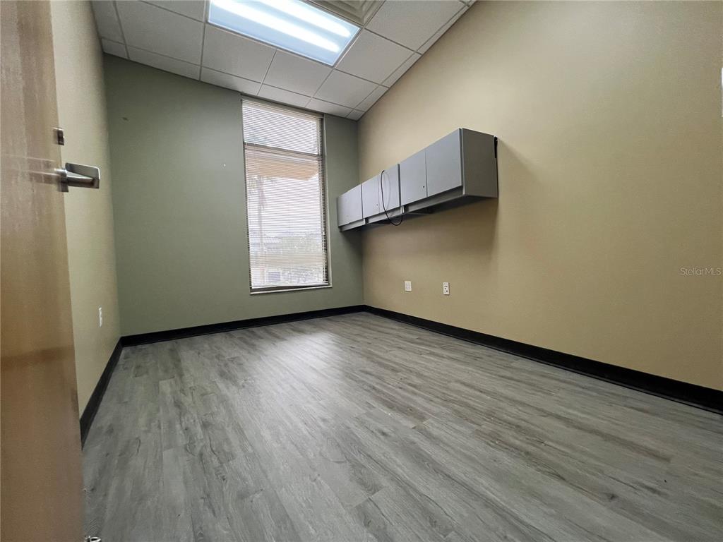 An empty office features light wood-look flooring, tan walls, a window, and wall-mounted cabinets — 800 CELEBRATION AVENUE UNIT 202-B, CELEBRATION, FL