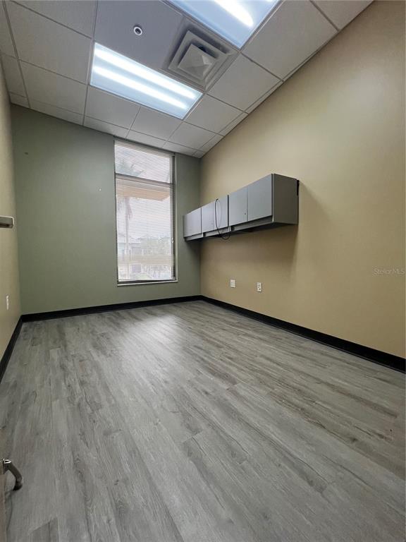 An empty office features light wood-look flooring, a window with blinds, and wall-mounted cabinets — 800 CELEBRATION AVENUE UNIT 202-B, CELEBRATION, FL