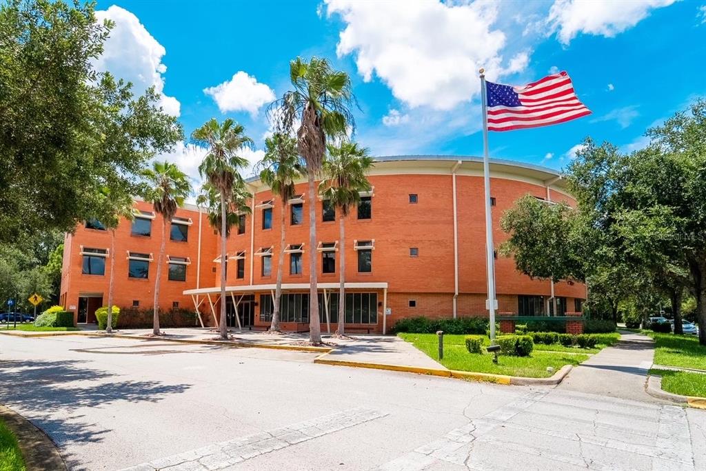A three-story brick building with a curved facade and palm trees stands under a blue sky — 800 CELEBRATION AVENUE UNIT 202-B, CELEBRATION, FL