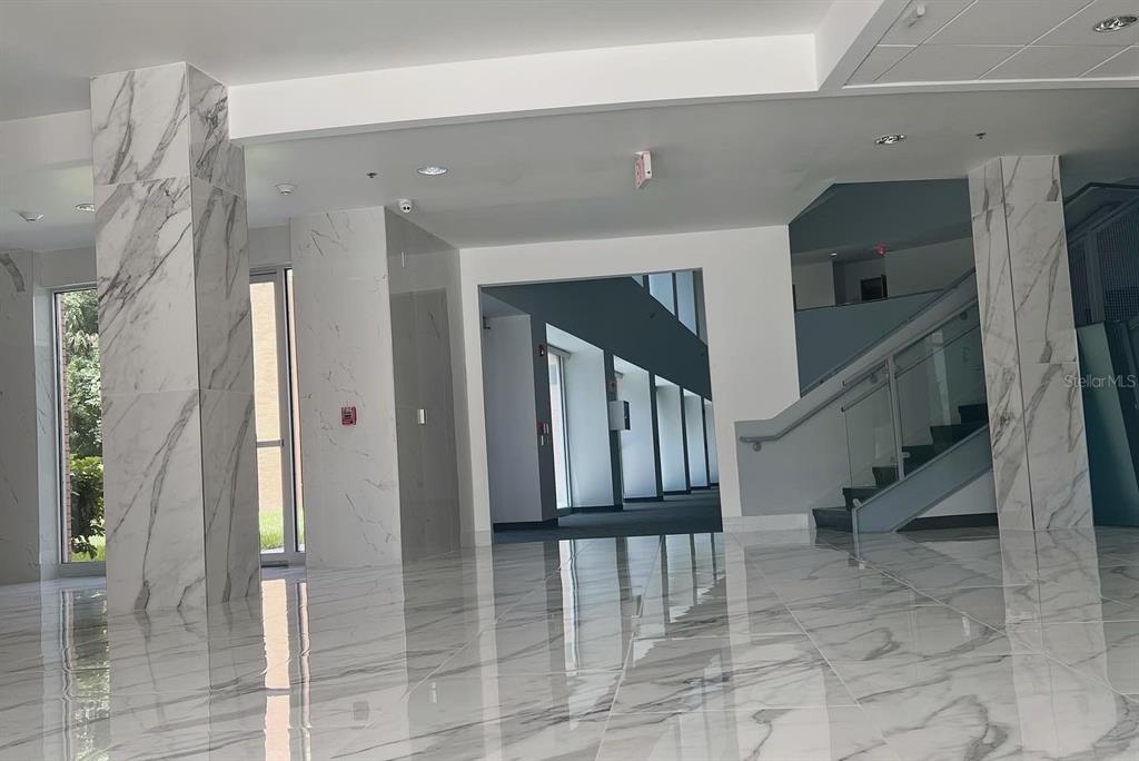 A modern lobby features white marble flooring, matching marble-clad pillars, and a glass-railed staircase — 800 CELEBRATION AVENUE UNIT 202-B, CELEBRATION, FL