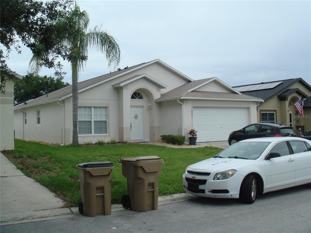 A single-story suburban house with a two-car garage, white stucco exterior, and a palm tree — 1036 CLEAR CREEK CIRCLE, CLERMONT, FL