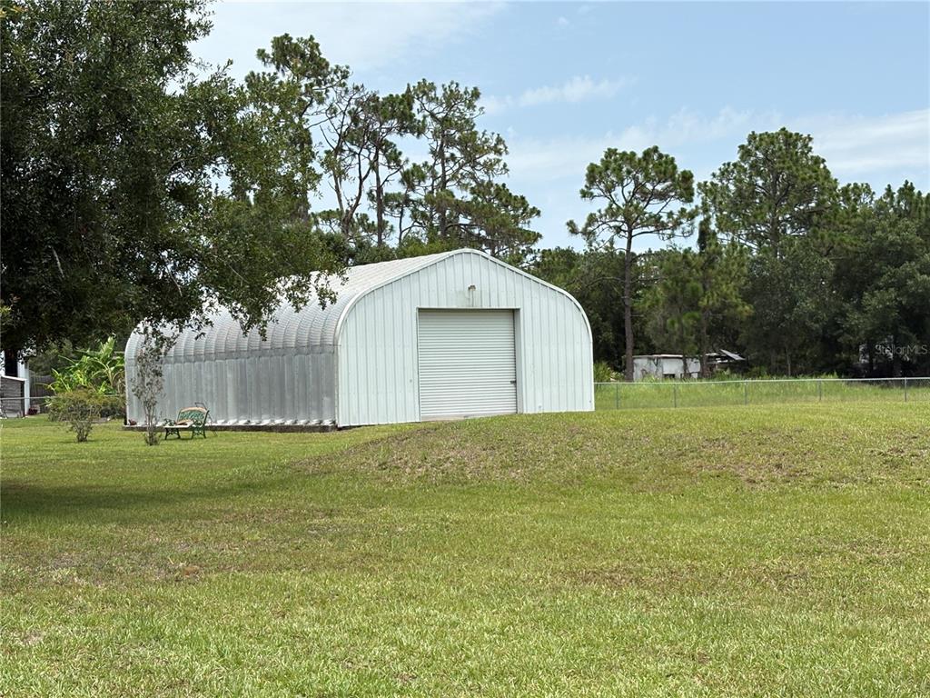 A metal Quonset hut building sits on a grassy lawn surrounded by trees — 9145 LINCOLN ROAD, ST CLOUD, FL