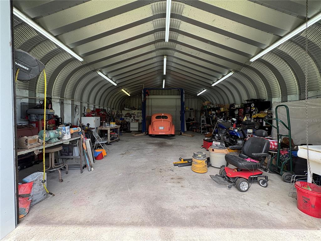 A large metal-sided workshop contains a car lift, a vintage orange car, and various tools — 9145 LINCOLN ROAD, ST CLOUD, FL