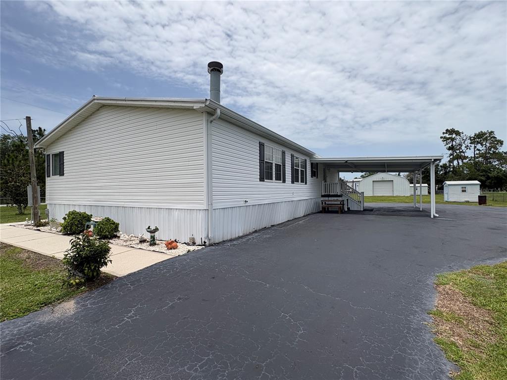 A white mobile home with a carport and a paved driveway under a cloudy sky — 9145 LINCOLN ROAD, ST CLOUD, FL