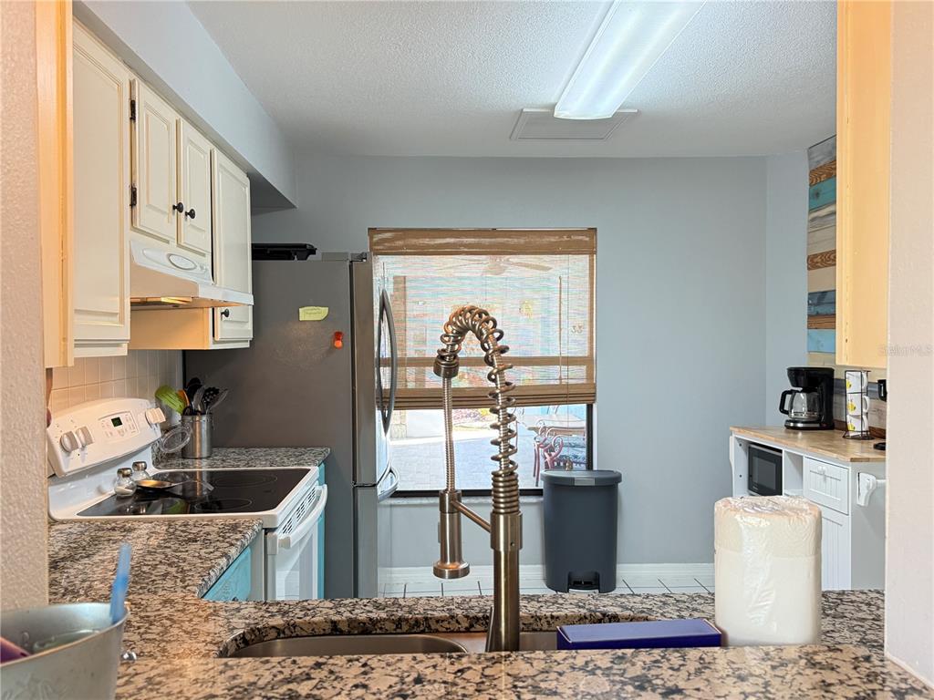A kitchen features granite countertops, white cabinets, a stainless steel refrigerator, and a sink faucet — 828 E 23RD AVENUE, NEW SMYRNA BEACH, FL