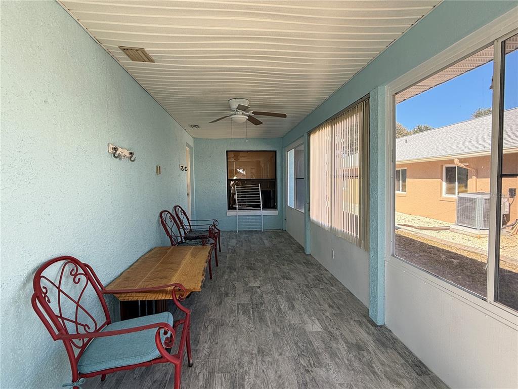 A covered patio features light blue walls, wood-look tile flooring, and red metal patio furniture — 828 E 23RD AVENUE, NEW SMYRNA BEACH, FL