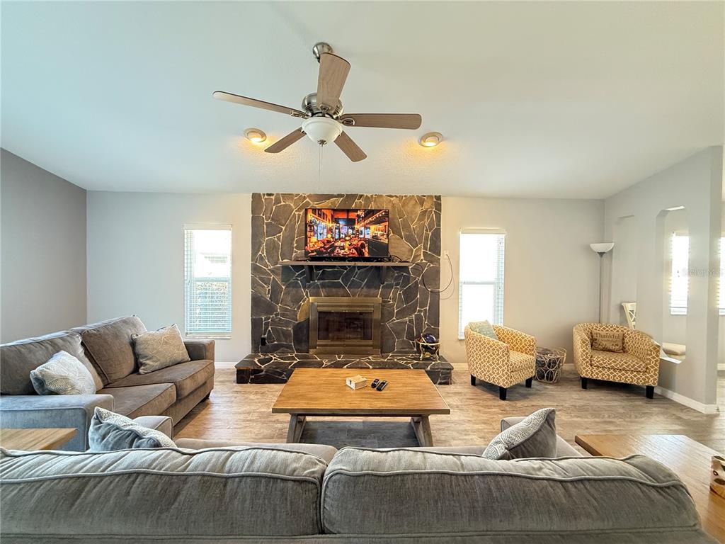 A living room features a stone fireplace, gray sofas, two patterned armchairs, and a ceiling fan — 828 E 23RD AVENUE, NEW SMYRNA BEACH, FL