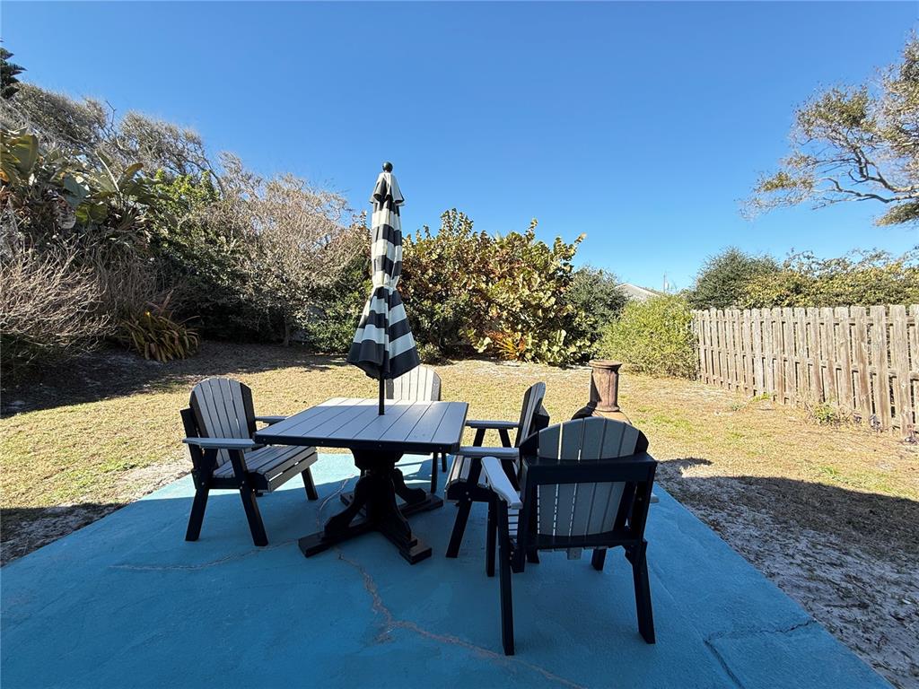 A patio with a table, chairs, and a striped umbrella sits in a grassy backyard — 828 E 23RD AVENUE, NEW SMYRNA BEACH, FL