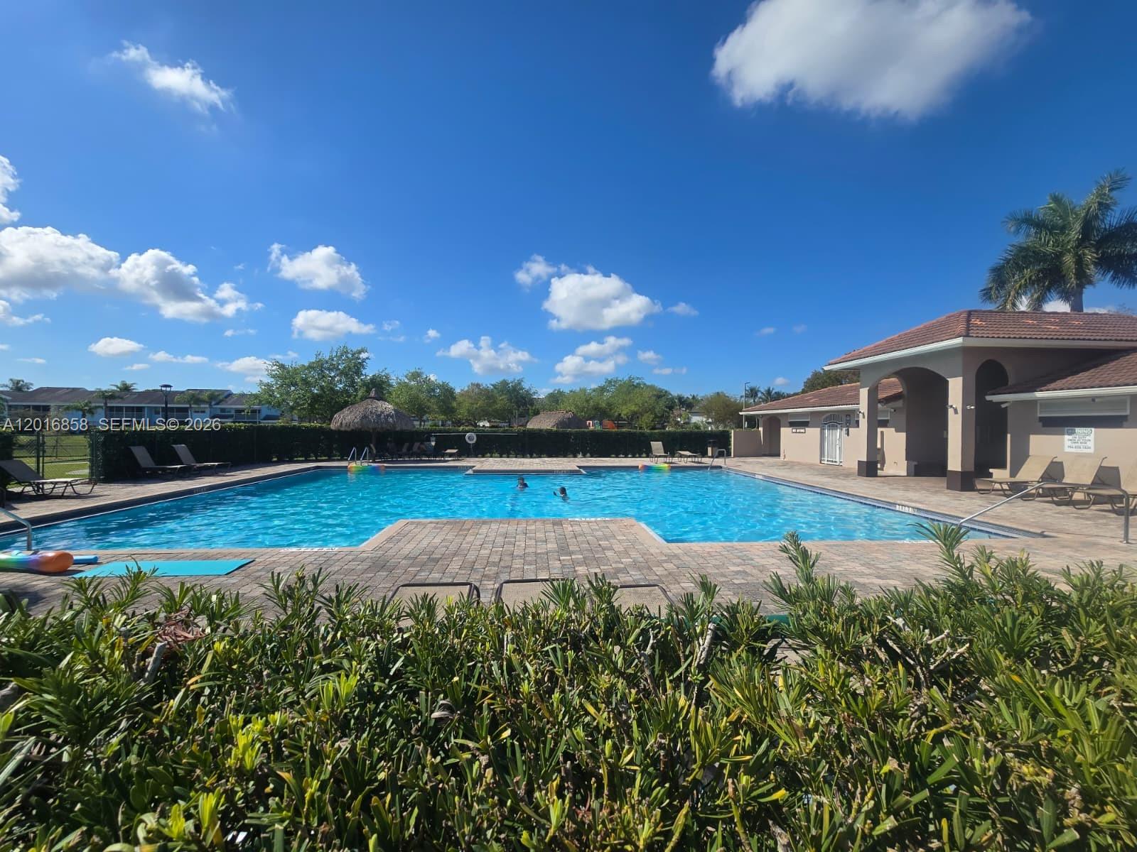 A rectangular swimming pool with a brick deck and a clubhouse under a blue sky — 1987 SE 23rd Rd, Homestead FL 33035, HOMESTEAD, FL