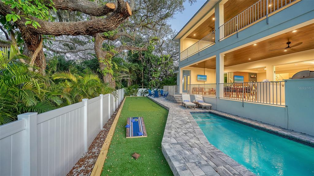 A backyard features a swimming pool, a putting green, and a cornhole game beside a house — 1537 SIESTA DRIVE, SARASOTA, FL