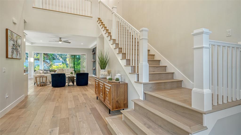 A bright entryway features light wood flooring, a staircase with white railings, and a living area — 1537 SIESTA DRIVE, SARASOTA, FL