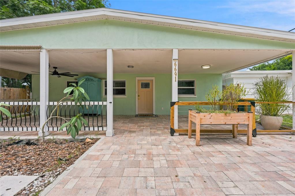 A light green house features a paved front patio with a covered carport and planter box — 6691 56TH AVENUE N, ST PETERSBURG, FL