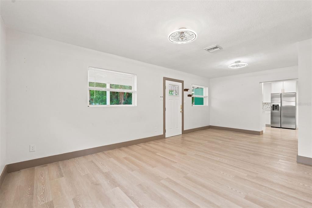 An empty living room with light wood-look flooring, white walls, and a view into the kitchen — 6691 56TH AVENUE N, ST PETERSBURG, FL