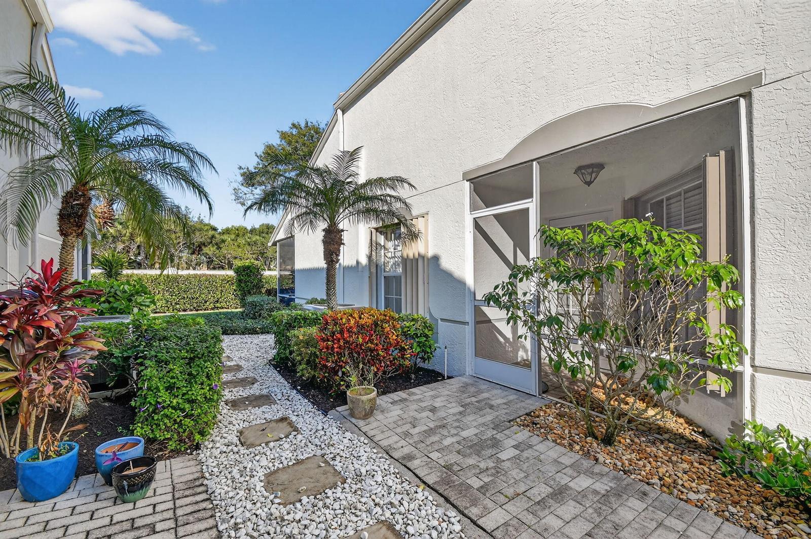 A paved walkway leads to a screened-in patio entrance beside a white stucco house exterior — 8536 Logia Circle, Boynton Beach FL 33472, BOYNTON BEACH, FL