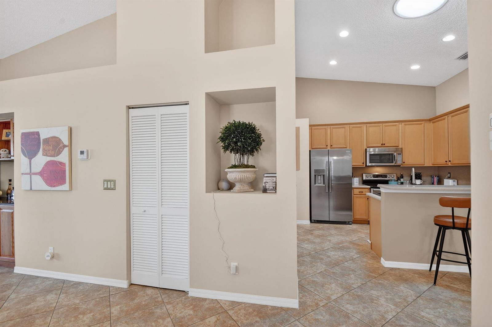 A kitchen with light wood cabinets and stainless steel appliances sits beside a tiled hallway — 8536 Logia Circle, Boynton Beach FL 33472, BOYNTON BEACH, FL