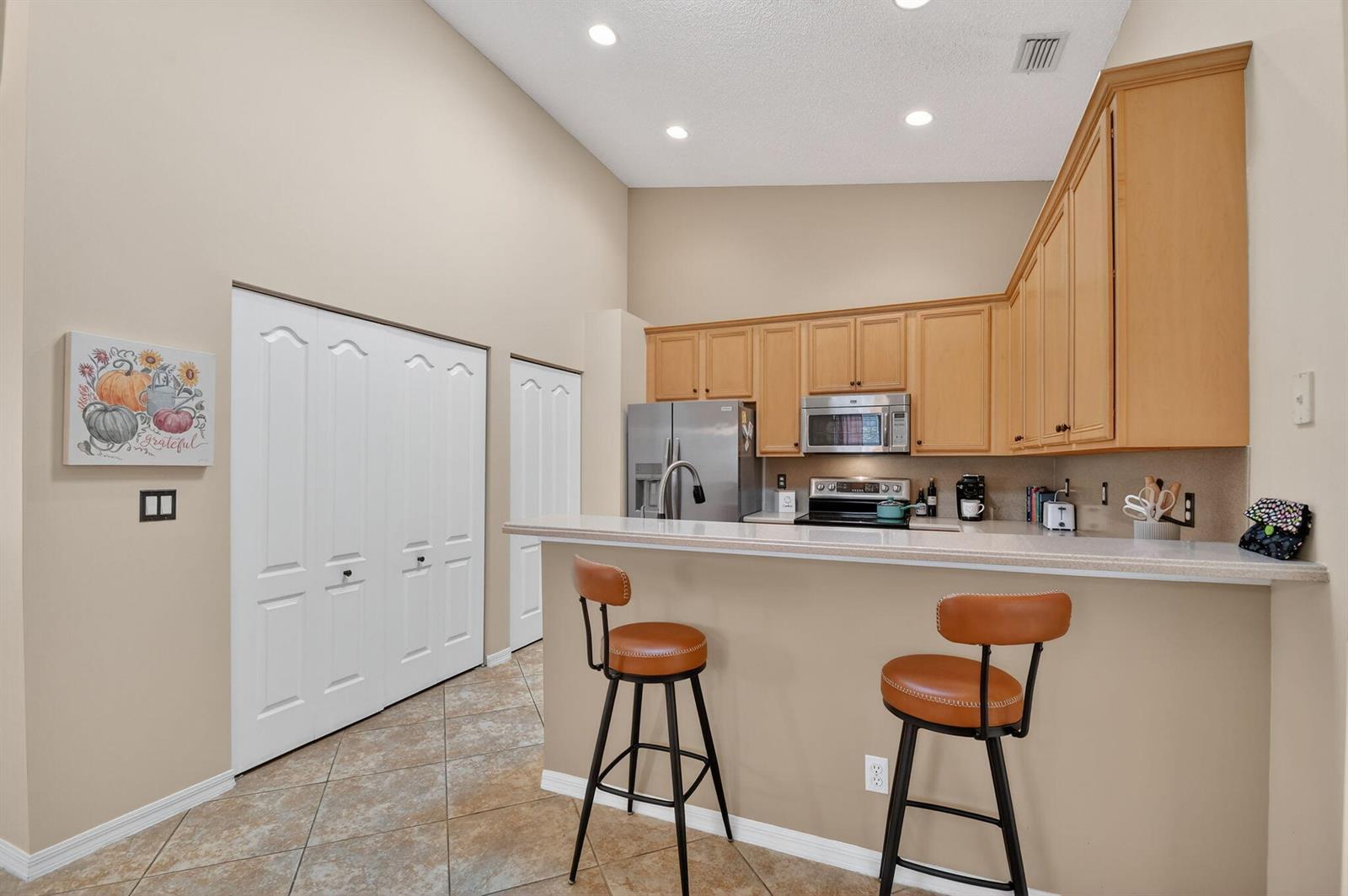 A kitchen features light wood cabinets, a breakfast bar with two stools, and tile flooring — 8536 Logia Circle, Boynton Beach FL 33472, BOYNTON BEACH, FL