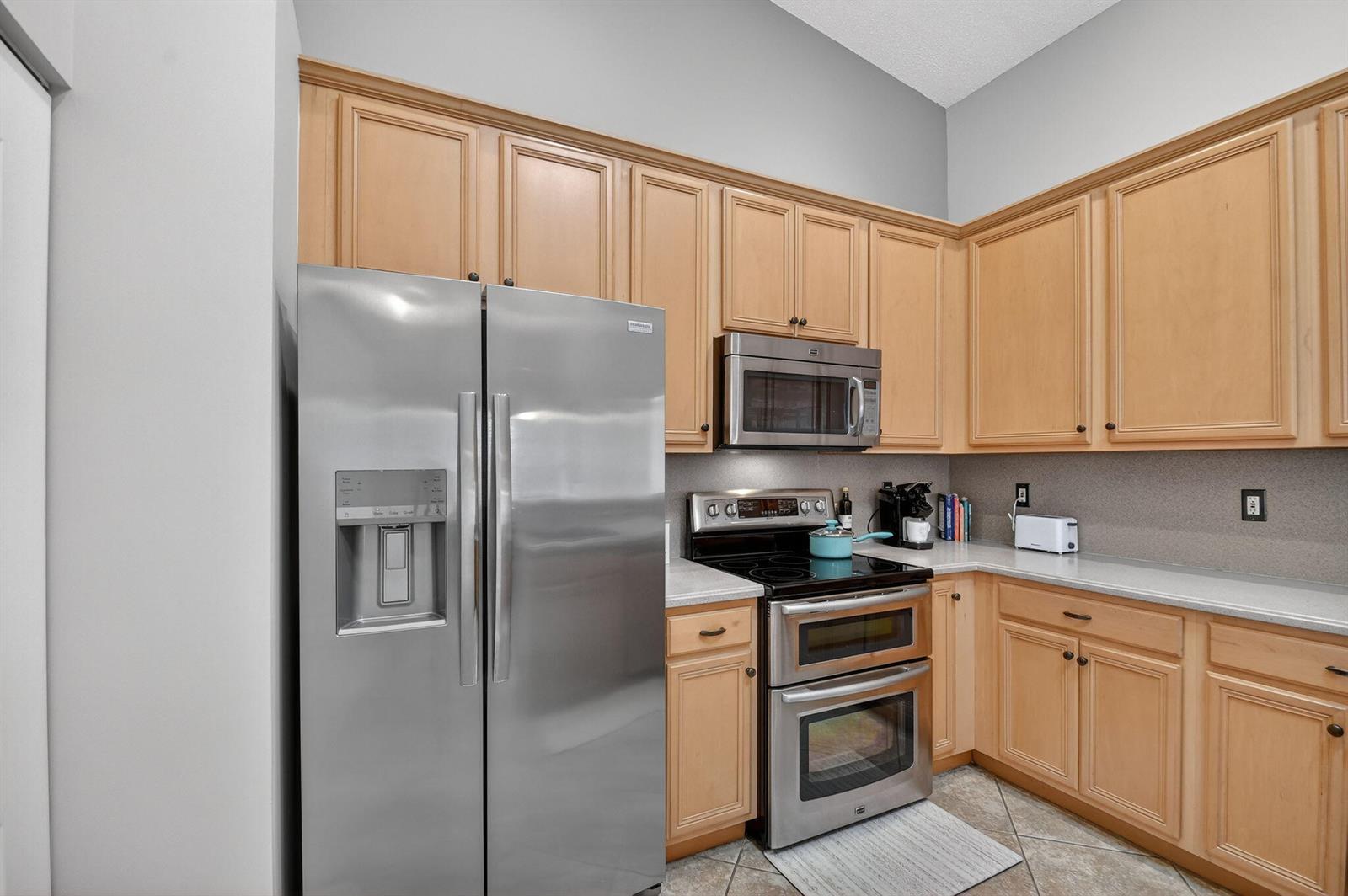 A kitchen features light wood cabinets, stainless steel appliances, and a gray countertop — 8536 Logia Circle, Boynton Beach FL 33472, BOYNTON BEACH, FL