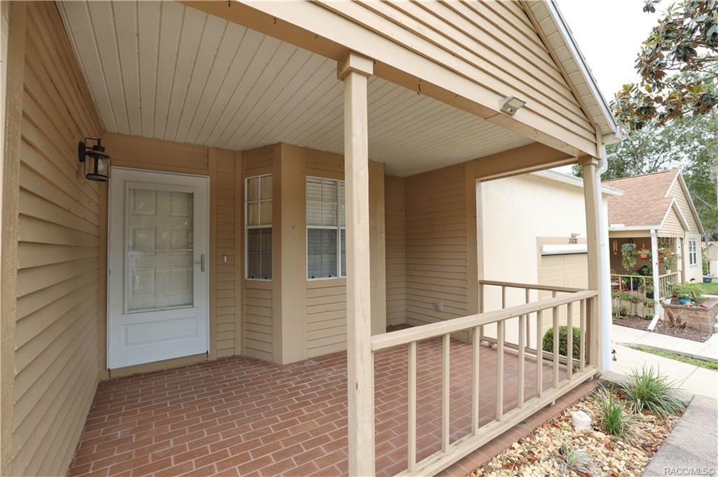 A covered porch with a brick floor, wooden railing, and a white front door — 3637 N LAURELWOOD LOOP, BEVERLY HILLS, FL