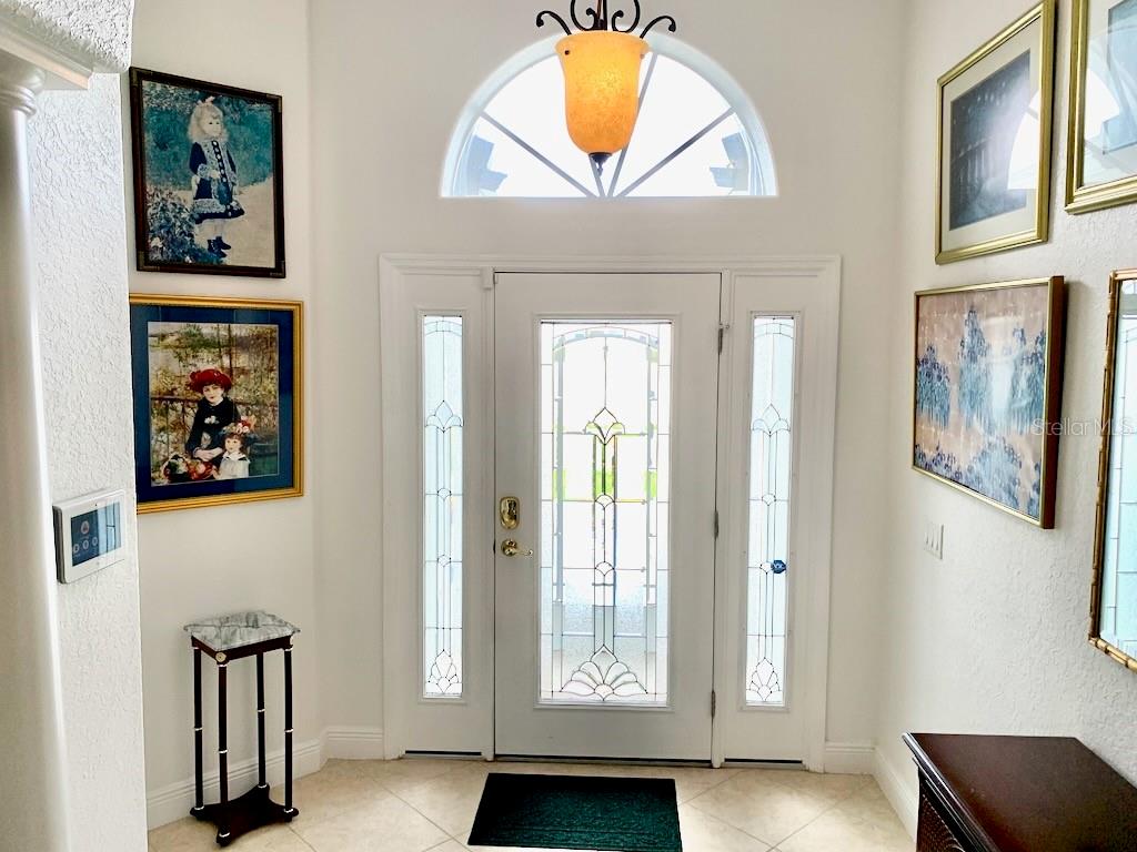 A bright entryway features a white front door with glass sidelights, tile flooring, and wall art — 24312 WESTGATE BOULEVARD, PUNTA GORDA, FL