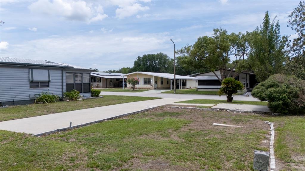 A view of a residential street with mobile homes, a concrete driveway, and grassy yards — 35100 COLONY HILLS DRIVE, ZEPHYRHILLS, FL