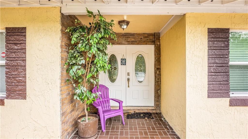 A covered front porch features a purple chair, a potted plant, and double entry doors — 2721 RAEFORD ROAD, ORLANDO, FL