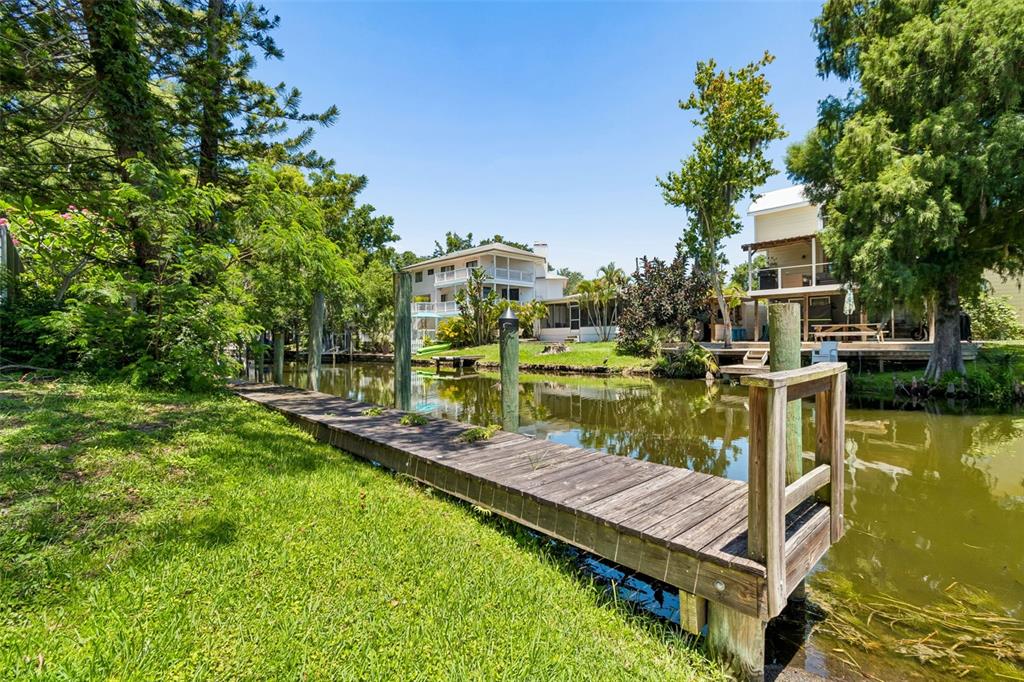 A wooden dock extends into a canal lined with trees and residential houses — 3141 N CANAL DRIVE, PALM HARBOR, FL