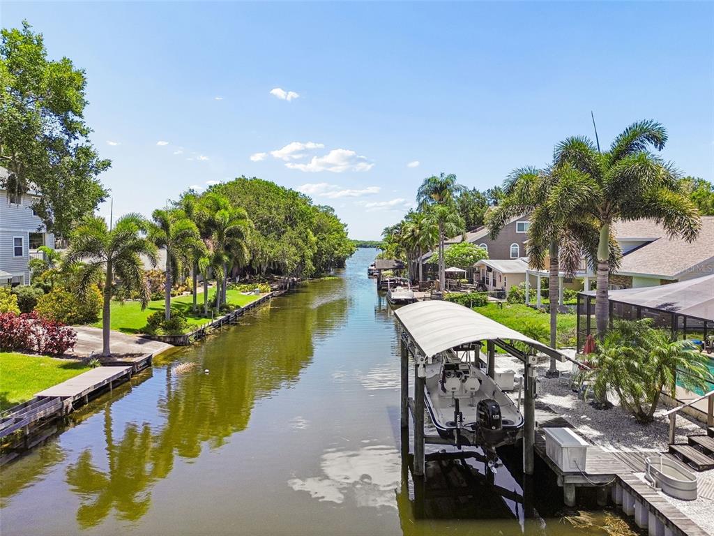 A canal view shows a boat under a covered lift with houses and palm trees — 3141 N CANAL DRIVE, PALM HARBOR, FL