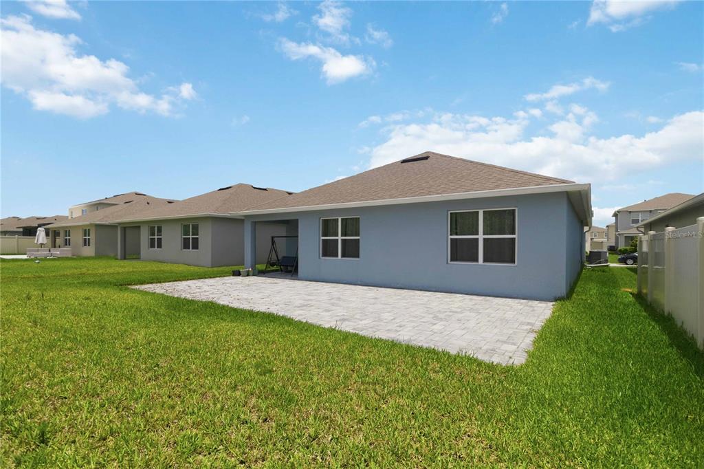 The back exterior of a light blue house features a paved patio and a grassy yard — 3198 EASTGROVE TERRACE, SANFORD, FL