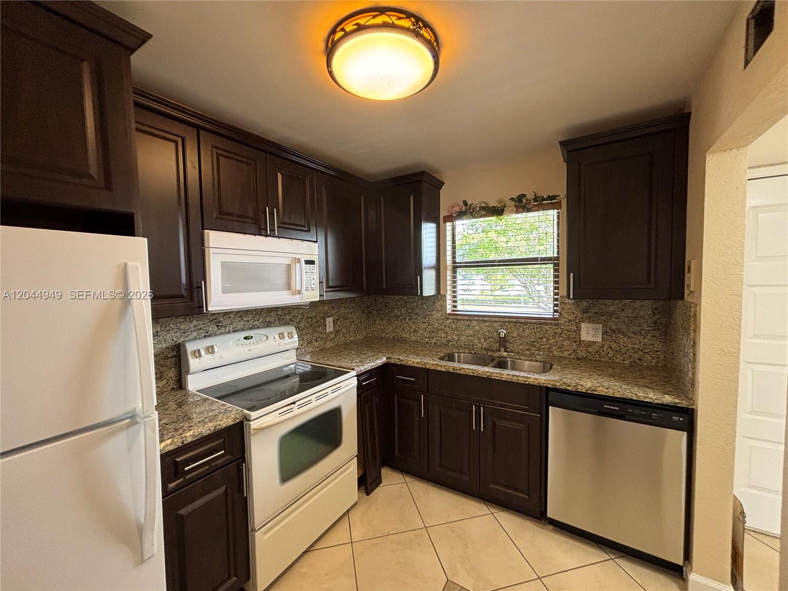 A kitchen features dark wood cabinets, granite countertops, white appliances, and tile flooring — 21909 Lake Forest Cir # 205, Boca Raton FL 33433, BOCA RATON, FL