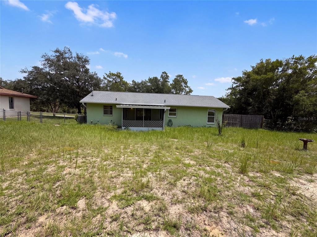 The exterior rear view of a light green house with a screened-in porch and yard — 3664 SW IVY PLACE, DUNNELLON, FL
