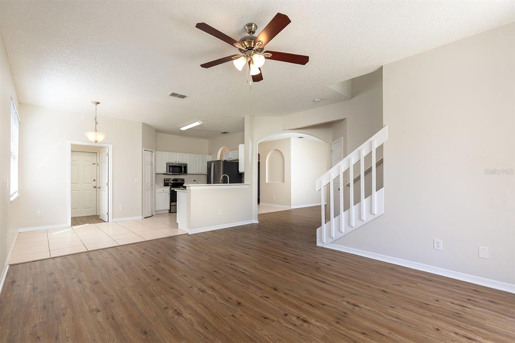 A living room with wood-look flooring, a ceiling fan, and an adjacent kitchen with tile — 4936 BELLTHORN DRIVE, ORLANDO, FL