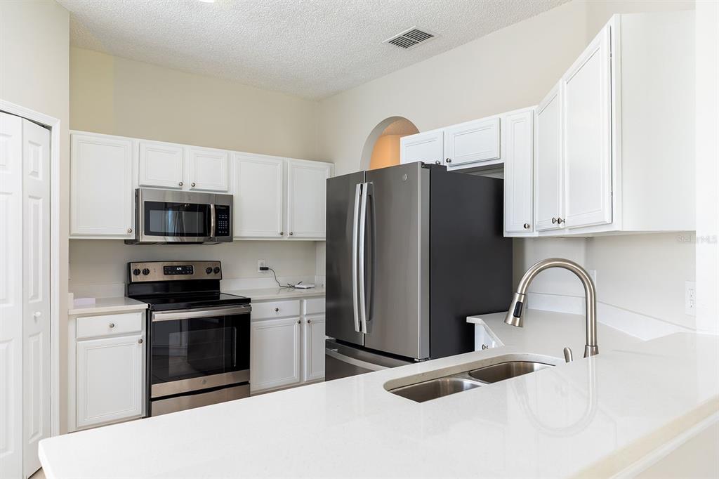 A kitchen with white cabinets, stainless steel appliances, and a white countertop with a sink — 4936 BELLTHORN DRIVE, ORLANDO, FL