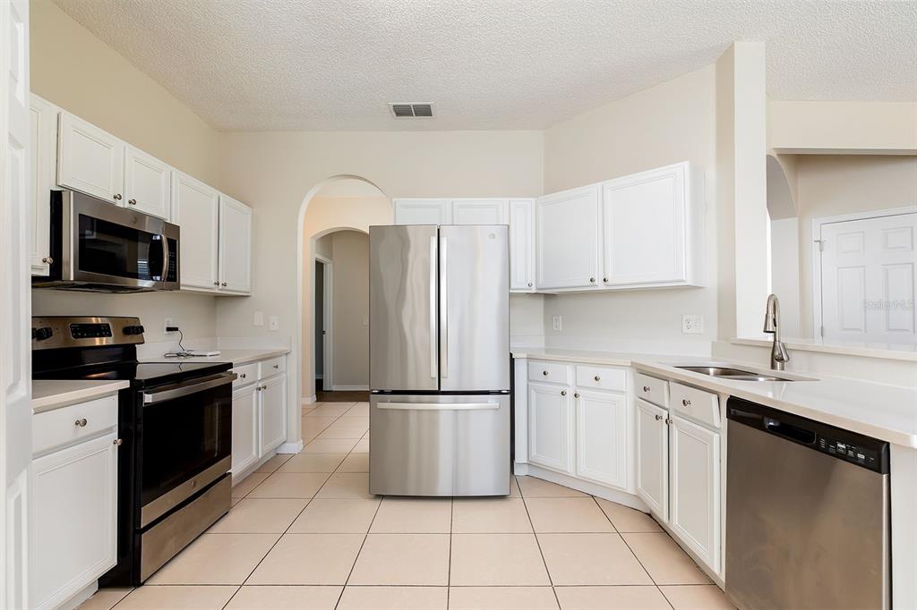 A kitchen features white cabinets, stainless steel appliances, and light-colored tile flooring — 4936 BELLTHORN DRIVE, ORLANDO, FL