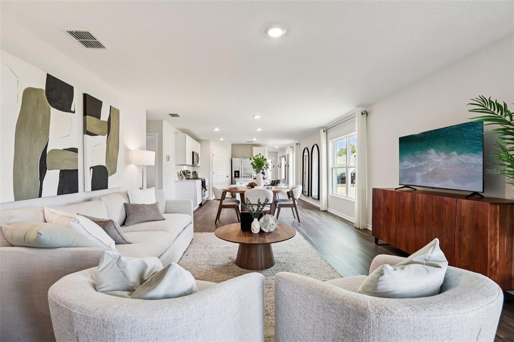 An open-concept living and dining area features light-colored furniture, dark wood flooring, and a television — 5172 PENELOPE TRAIL, LAKELAND, FL
