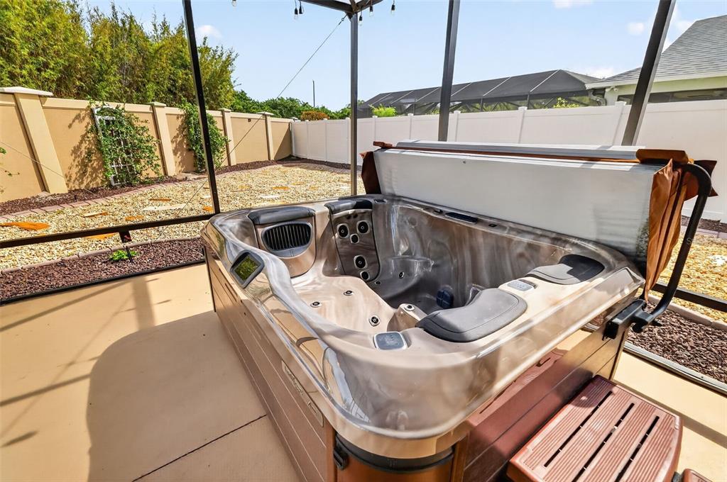 A hot tub sits on a concrete patio inside a screened-in enclosure with gravel landscaping — 2873 CHARLEVOIX STREET, THE VILLAGES, FL