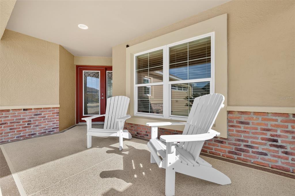 A covered porch features two white Adirondack chairs, a red front door, and brick accents — 2873 CHARLEVOIX STREET, THE VILLAGES, FL