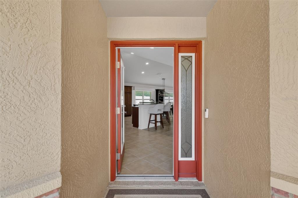 An open front door reveals a kitchen with a center island and bar stools inside — 2873 CHARLEVOIX STREET, THE VILLAGES, FL
