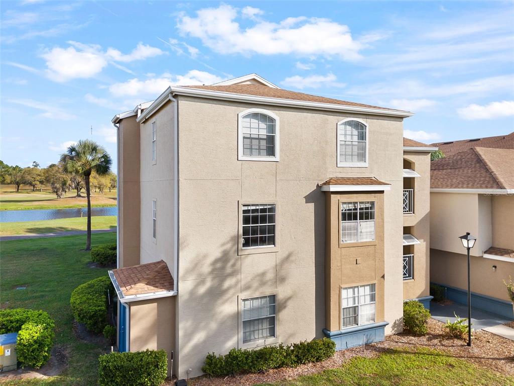 An exterior view of a three-story tan stucco apartment building with a brown shingled roof — 7320 WESTPOINTE BOULEVARD UNIT 533, ORLANDO, FL