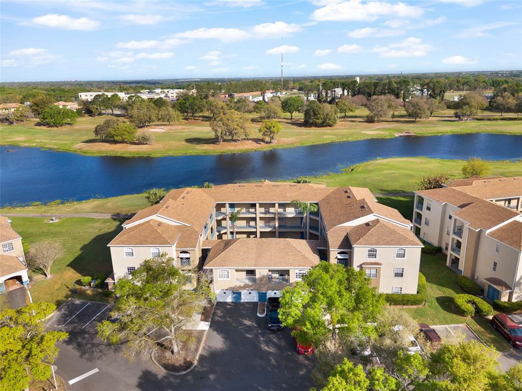 An aerial view shows a multi-story apartment building situated next to a golf course pond — 7320 WESTPOINTE BOULEVARD UNIT 533, ORLANDO, FL