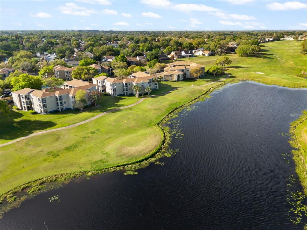 An aerial view shows apartment buildings situated along a golf course next to a lake — 7320 WESTPOINTE BOULEVARD UNIT 533, ORLANDO, FL
