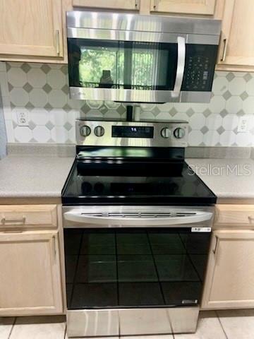 A kitchen features light wood cabinets, stainless steel appliances, a breakfast bar, and two stools — 8939 LATREC AVENUE UNIT 1307, ORLANDO, FL
