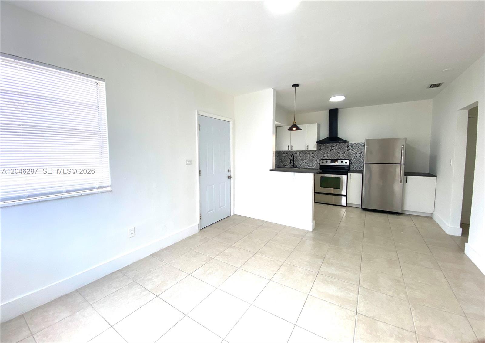 A kitchen with white cabinets and stainless steel appliances opens into a tiled living area — 120 NE 55th St # 5, Miami FL 33137, MIAMI, FL