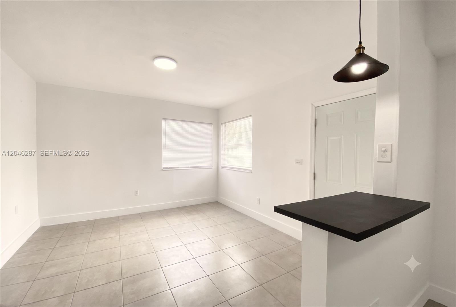 A bright, tiled room features white walls, two windows, and a black kitchen counter — 120 NE 55th St # 5, Miami FL 33137, MIAMI, FL