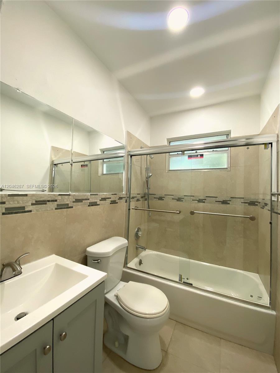 A bathroom features a white vanity, a toilet, and a bathtub with a glass enclosure — 120 NE 55th St # 5, Miami FL 33137, MIAMI, FL