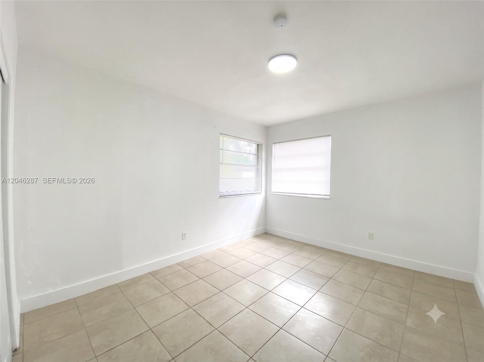 An empty room features white walls, light-colored tile flooring, and two windows with blinds — 120 NE 55th St # 5, Miami FL 33137, MIAMI, FL