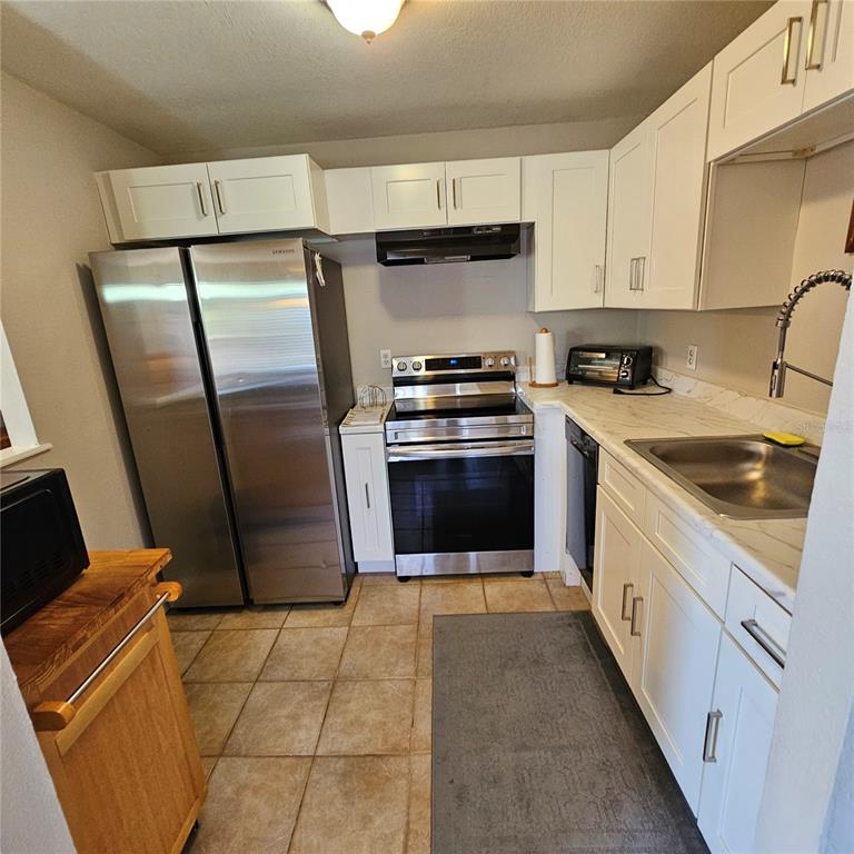 A kitchen features white cabinets, stainless steel appliances, a sink, and light-colored tile flooring — 301 ANDOVER PLACE S UNIT 175, SUN CITY CENTER, FL